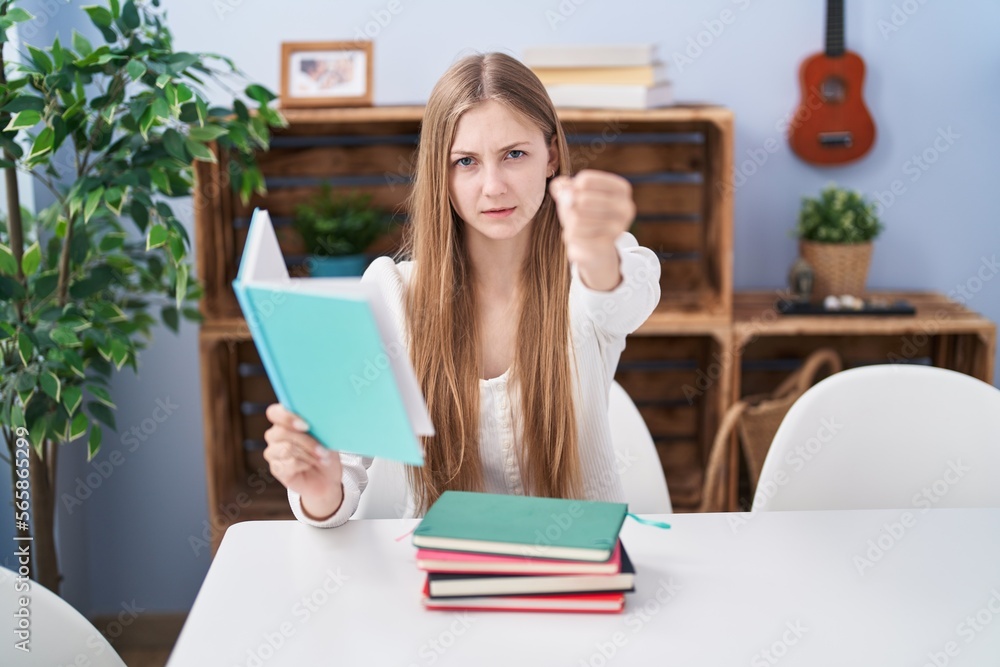 Young caucasian woman reading books at home annoyed and frustrated shouting with anger, yelling crazy with anger and hand raised Young caucasian woman reading books at home annoyed and frustrated shouting with anger, yelling crazy with anger and hand raised