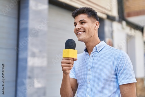 Young hispanic man reporter working using microphone at street