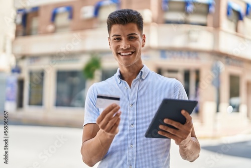 Young hispanic man using touchpad and credit card at street