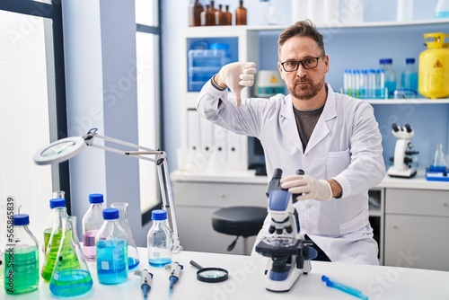 Middle age caucasian man working at scientist laboratory with angry face  negative sign showing dislike with thumbs down  rejection concept