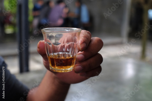 Close up of a person's hand holding a small transparent glass filled with vodka.