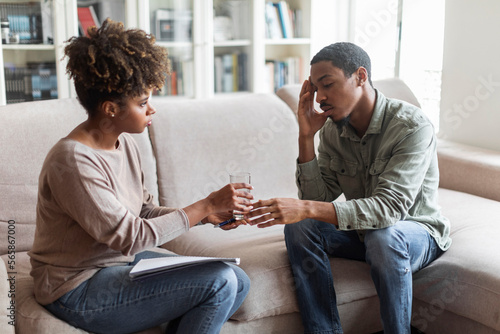 African woman psychotherapist give male patient glass of water