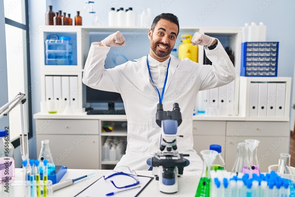 Young hispanic man with beard working at scientist laboratory showing arms muscles smiling proud. fitness concept. Young hispanic man with beard working at scientist laboratory showing arms muscles smiling proud. fitness concept.