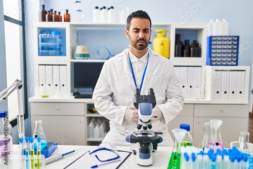 Young hispanic man with beard working at scientist laboratory with hand on stomach because nausea  painful disease feeling unwell. ache concept.
