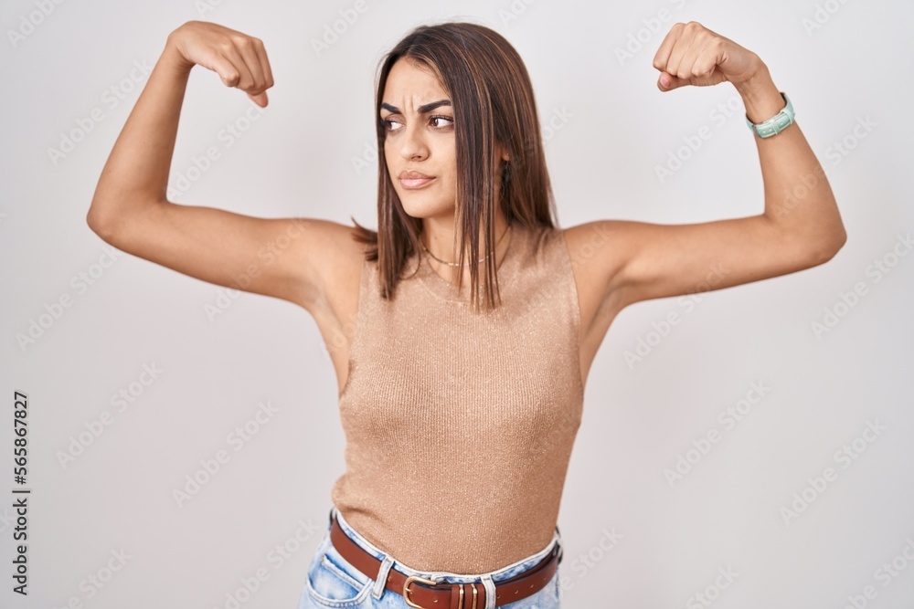 Obraz premium Young hispanic woman standing over white background showing arms muscles smiling proud. fitness concept.