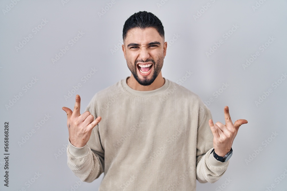 Young handsome man standing over isolated background shouting with crazy expression doing rock symbol with hands up. music star. heavy music concept. Young handsome man standing over isolated background shouting with crazy expression doing rock symbol with hands up. music star. heavy music concept.