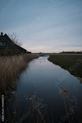 Canal on field by house against sky during dusk photo