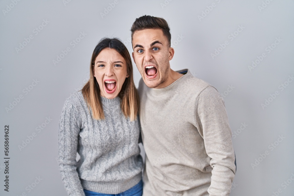Young hispanic couple standing over white background angry and mad screaming frustrated and furious, shouting with anger. rage and aggressive concept. Young hispanic couple standing over white background angry and mad screaming frustrated and furious, shouting with anger. rage and aggressive concept.