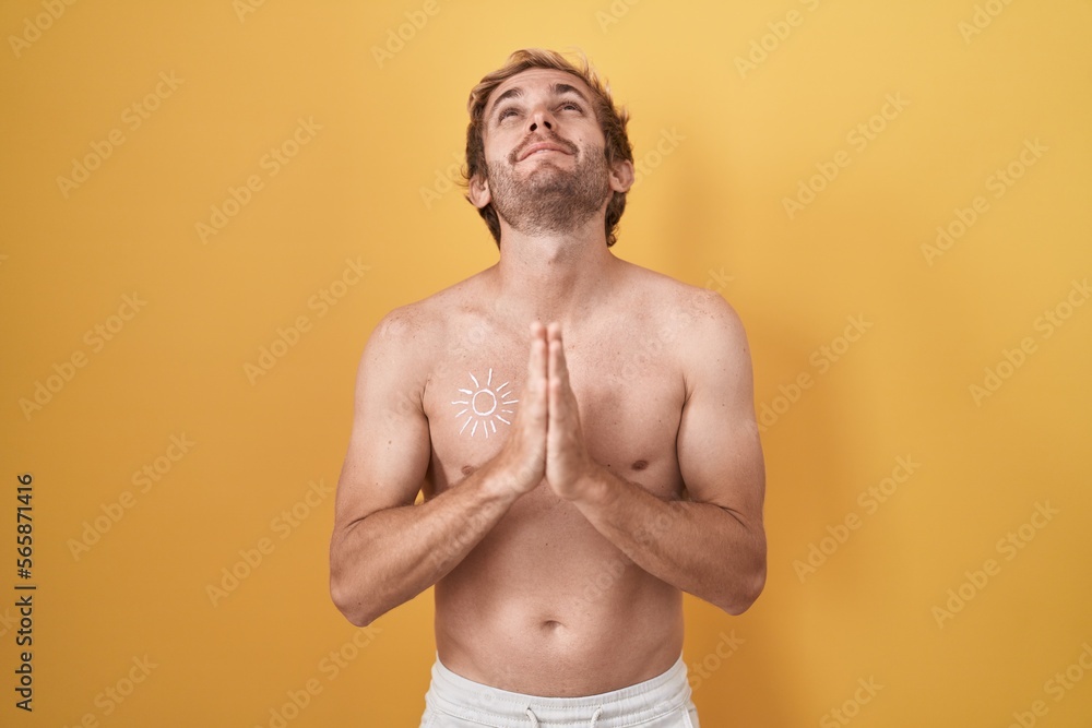 Caucasian man standing shirtless wearing sun screen begging and praying with hands together with hope expression on face very emotional and worried. begging.