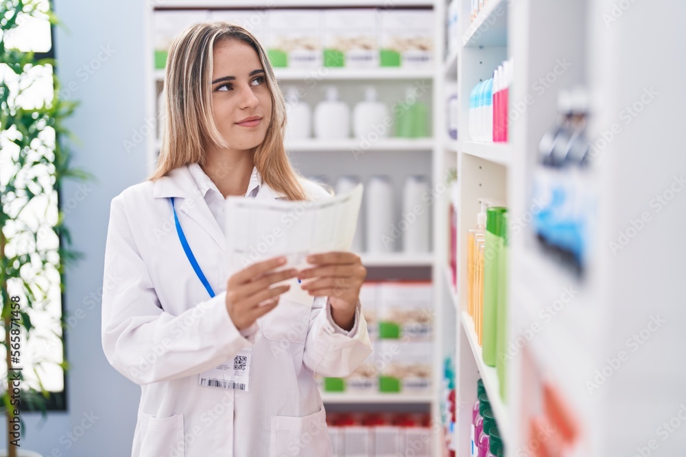 Young blonde woman pharmacist reading prescription at pharmacy