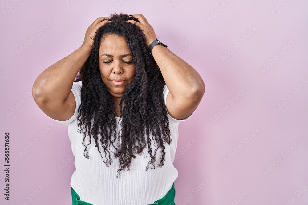 Plus size hispanic woman standing over pink background suffering from headache desperate and stressed because pain and migraine. hands on head. Plus size hispanic woman standing over pink background suffering from headache desperate and stressed because pain and migraine. hands on head.