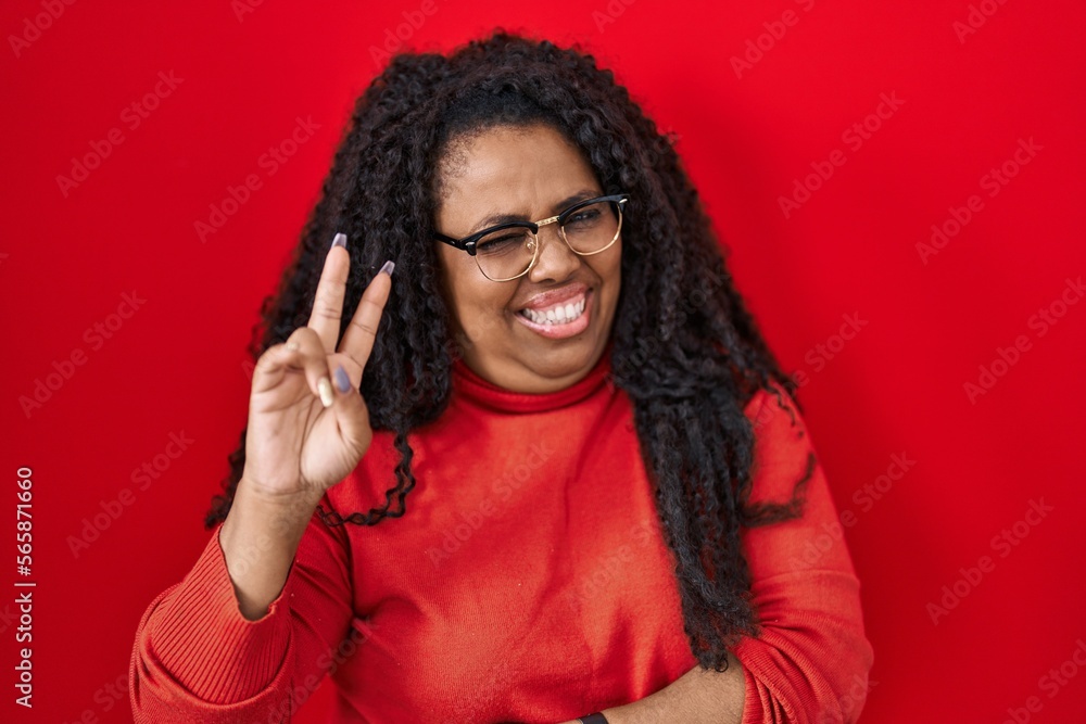 Plus size hispanic woman standing over red background smiling looking to the camera showing fingers doing victory sign. number two. Plus size hispanic woman standing over red background smiling looking to the camera showing fingers doing victory sign. number two.