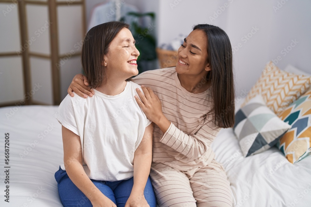 Two women mother and daughter hugging each other sitting on bed at bedroom Two women mother and daughter hugging each other sitting on bed at bedroom