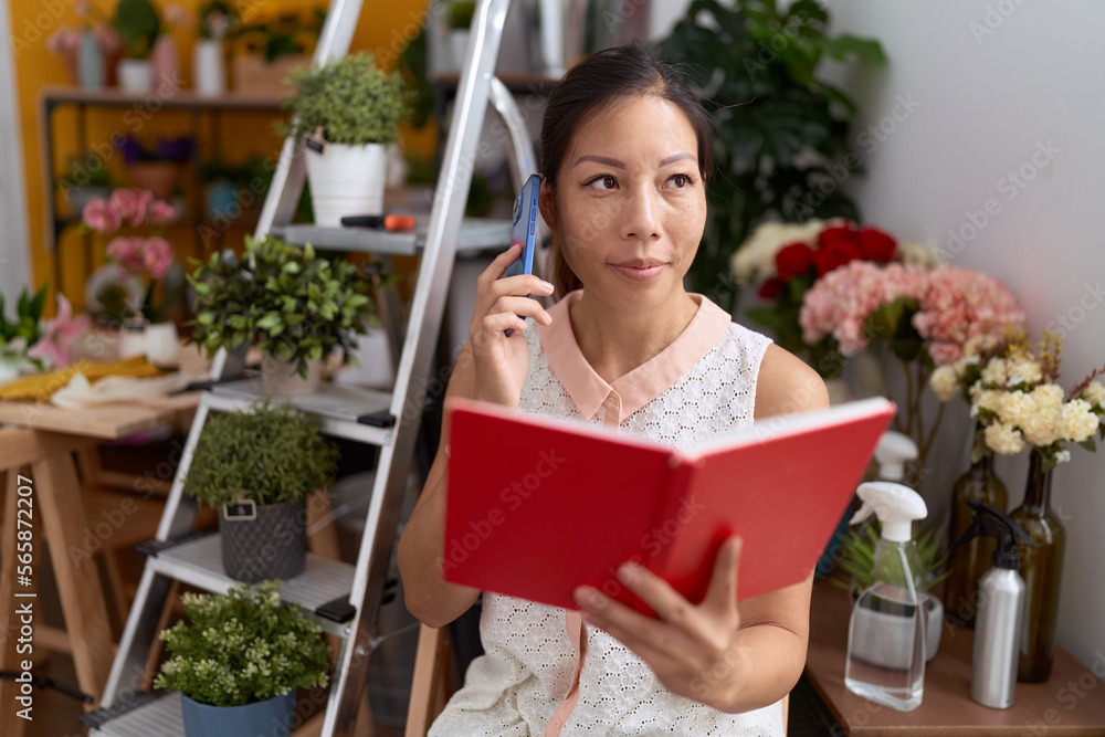 Young asian woman florist talking on smartphone reading book at flower shop