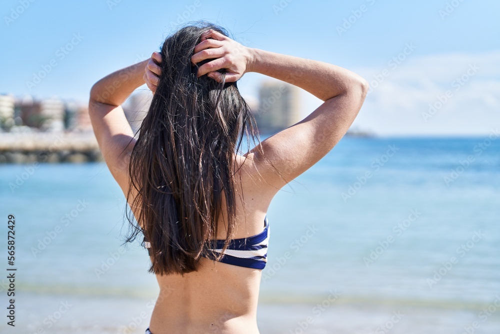 Naklejka premium Young hispanic woman wearing bikini standing at seaside