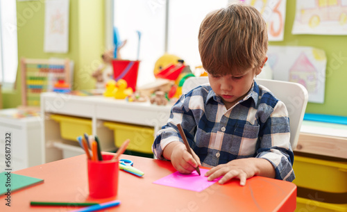 Adorable hispanic boy preschool student sitting on table drawing on paper at kindergarten