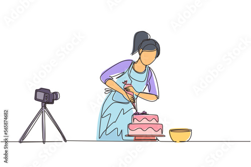 Single continuous line drawing girl baking and decorating cake at kitchen. Woman blogger recording video on camera, using tripod, posting it on social media. One line draw design vector illustration