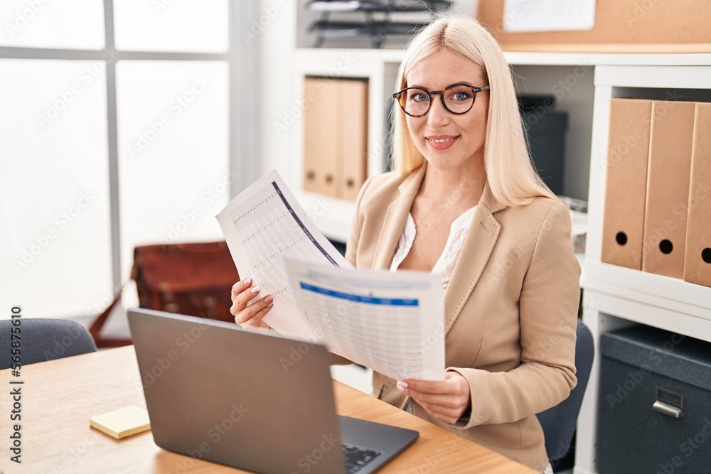 Young blonde woman business worker using laptop working and reading document at office Young blonde woman business worker using laptop working and reading document at office