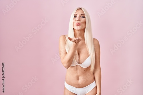 Caucasian woman wearing lingerie over pink background looking at the camera blowing a kiss with hand on air being lovely and sexy. love expression.