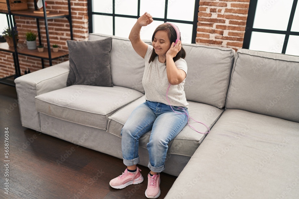 Obraz premium Down syndrome woman listening to music and dancing sitting on sofa at home