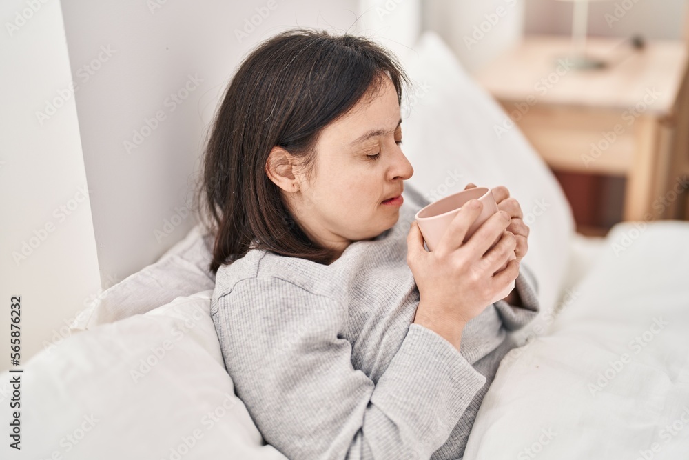 Young woman with down syndrome drinking cup of coffee sitting on bed at bedroom Young woman with down syndrome drinking cup of coffee sitting on bed at bedroom