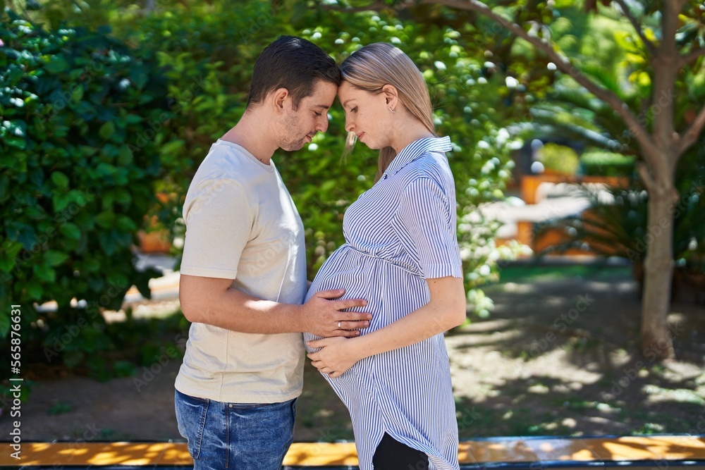 Man and woman couple standing together touching belly at park Man and woman couple standing together touching belly at park