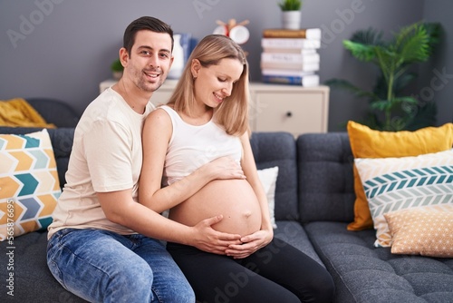 Man and woman couple touching belly sitting on sofa at home