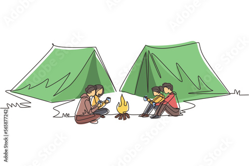 Continuous one line drawing two couple camping around campfire tents. Group of man woman sitting on ground and drinking hot tea getting warm near bonfire. Single line draw design vector illustration