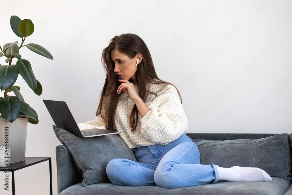 An attractive freelance woman is sitting on the couch and using a laptop to work online. An attractive freelance woman is sitting on the couch and using a laptop to work online.