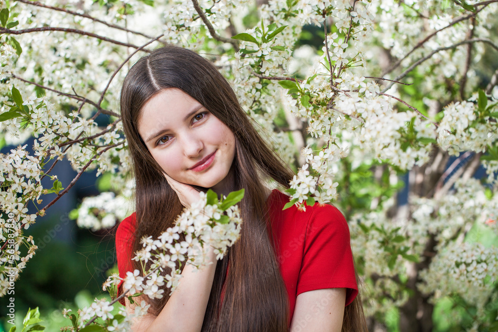 Pretty teen girl are posing in garden near blossom cherry tree with white flowers