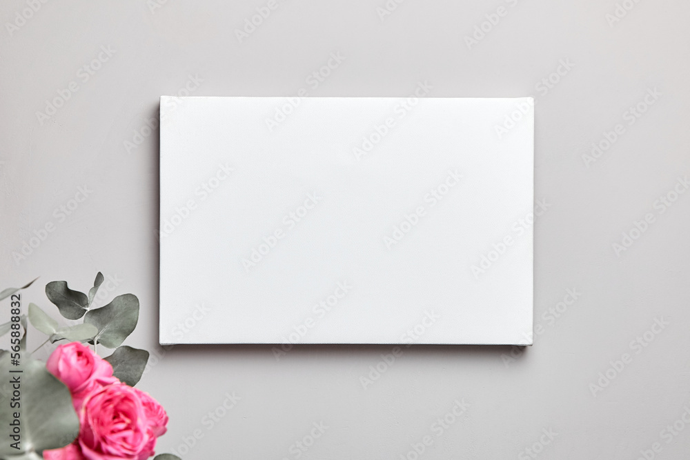 Blank canvas mockup hanging on grey wall and pink flowers in interior. White canvas and floral decor Blank canvas mockup hanging on grey wall and pink flowers in interior. White canvas and floral decor