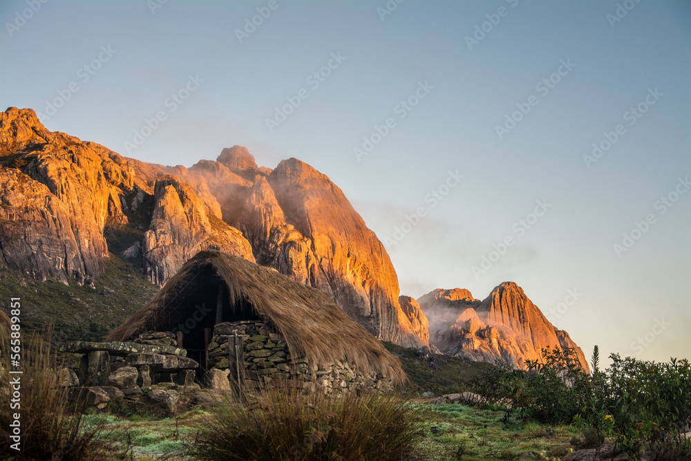 Andringitra National Park during the sunrise. Stone hut with tratched roof with rocky mountaind in the background with morning sun. Madagascar. 