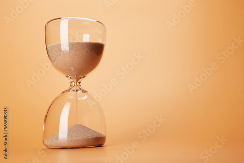 Hourglass with clean sand pouring down countdown the time, isolated on the bright solid fond plain sandy beige background