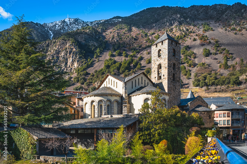 Beautiful, 11th century stone St. Esteve Church surrounded by green trees with Pyrenees Mountains in background, Andorra la Vella