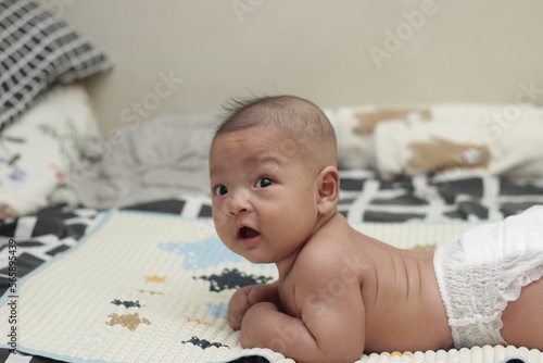 A 3 month old Asian baby wearing diapers is trying to learn to crawl on a mattress. Selective focus
