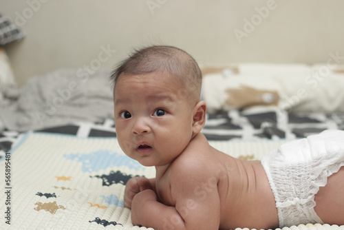 A 3 month old Asian baby wearing diapers is trying to learn to crawl on a mattress. Selective focus