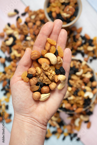 natural background of different types of nuts is held in the hand and scattered on the table. Nuts almonds, walnuts, hazelnuts and light and dark raisins