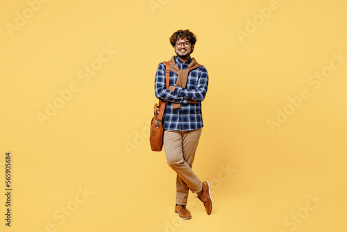 Full body young teacher confident serious calm teen Indian boy IT student wear casual clothes shirt glasses bag look camera isolated on plain yellow color background. High school university concept.