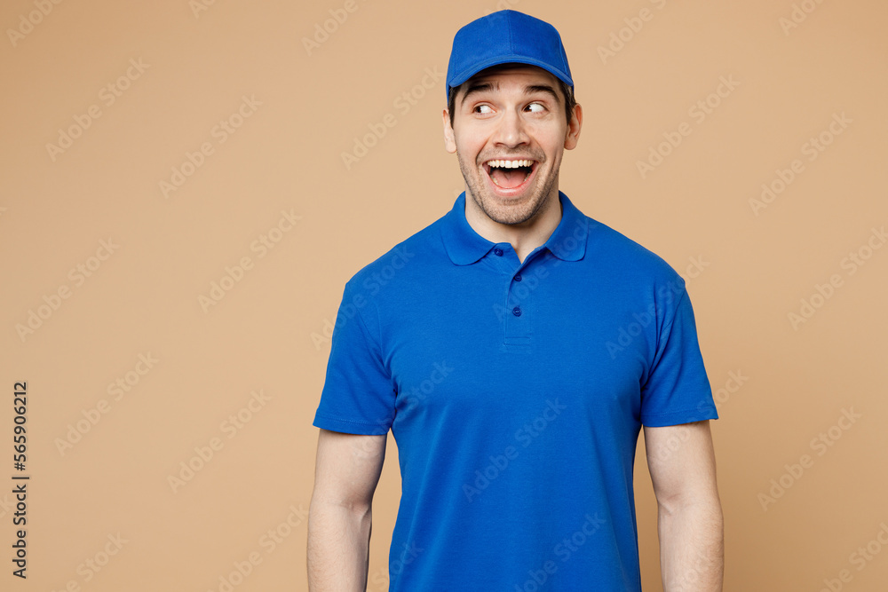 Professional surprised delivery guy employee man wear blue cap t-shirt uniform workwear work as dealer courier look aside on workspace area isolated on plain light beige background. Service concept.