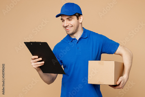 Delivery guy employee man wearing blue cap t-shirt uniform workwear work as dealer courier hold clipboard with papers document cardboard box isolated on plain light beige background. Service concept. photo