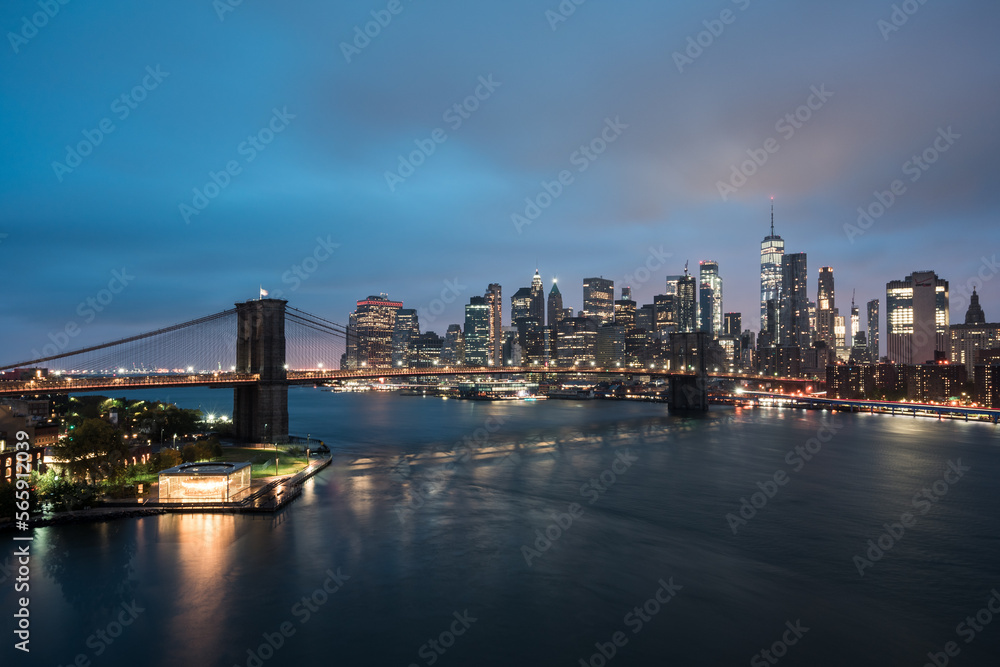 Skyline von New York in der Dämmerung mit Brooklyn Bridge und Lichtern am Fluss.