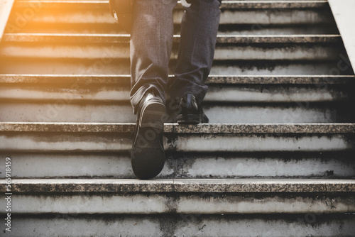 Step to success concept Sucessful business man walking up stairs Businessman with bags in his hands walking stairs going to office in the morning Elegant man in suit taking steps with sunlgiht