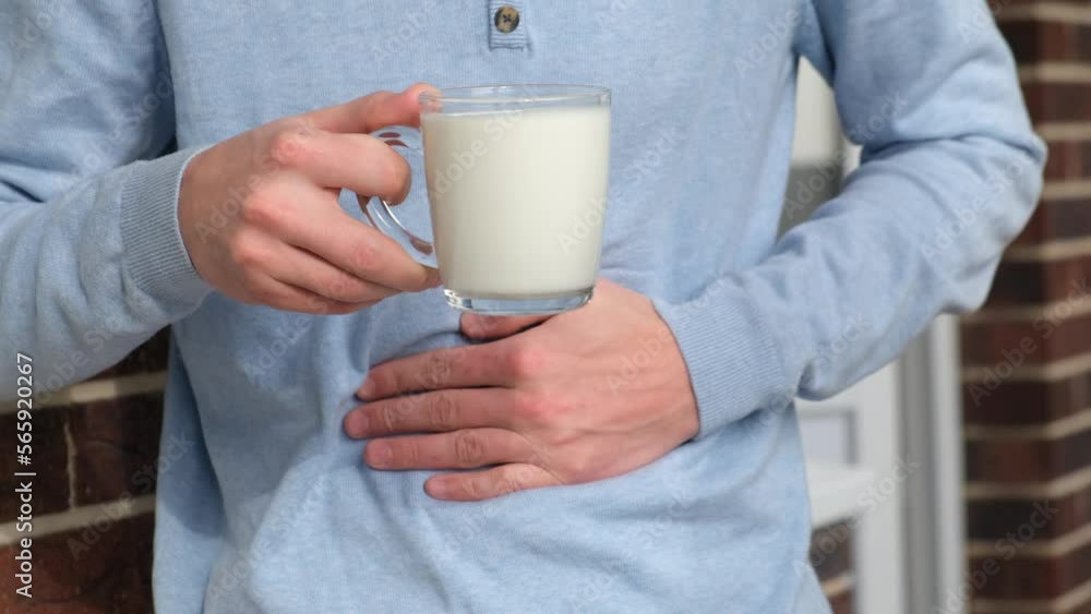 Lactose intolerance. A man with a glass of milk holds his stomach feeling discomfort Lactose intolerance. A man with a glass of milk holds his stomach feeling discomfort