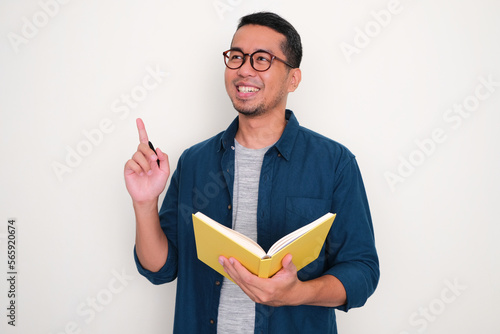 Adult Asian man showing got new idea pose while holding a book and pen photo