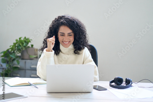 Happy euphoric young woman student or employee, office worker winner using laptop computer celebrating marketing goal winning online getting good news in email raising hands feeling excited.