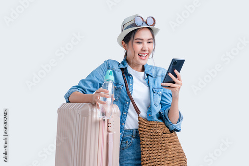ready to travel ,asian smiling cheerful female woman hand using smartphone check flight schedule pull luggage bag prepare to new abroad journey travel studio shot on white background 