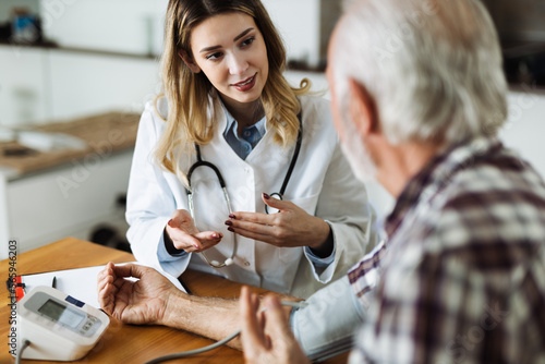 Female doctor measuring blood pressure of a senior man during a home visit photo