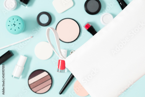 Set of different makeup cosmetics on blue background. White makeup bag and cosmetic beauty products. Flat lay, top view, copy space