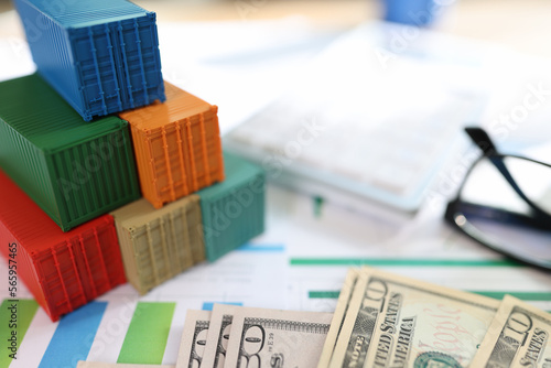 Several colorful cargo containers with us dollar bills and glasses on financial reports.