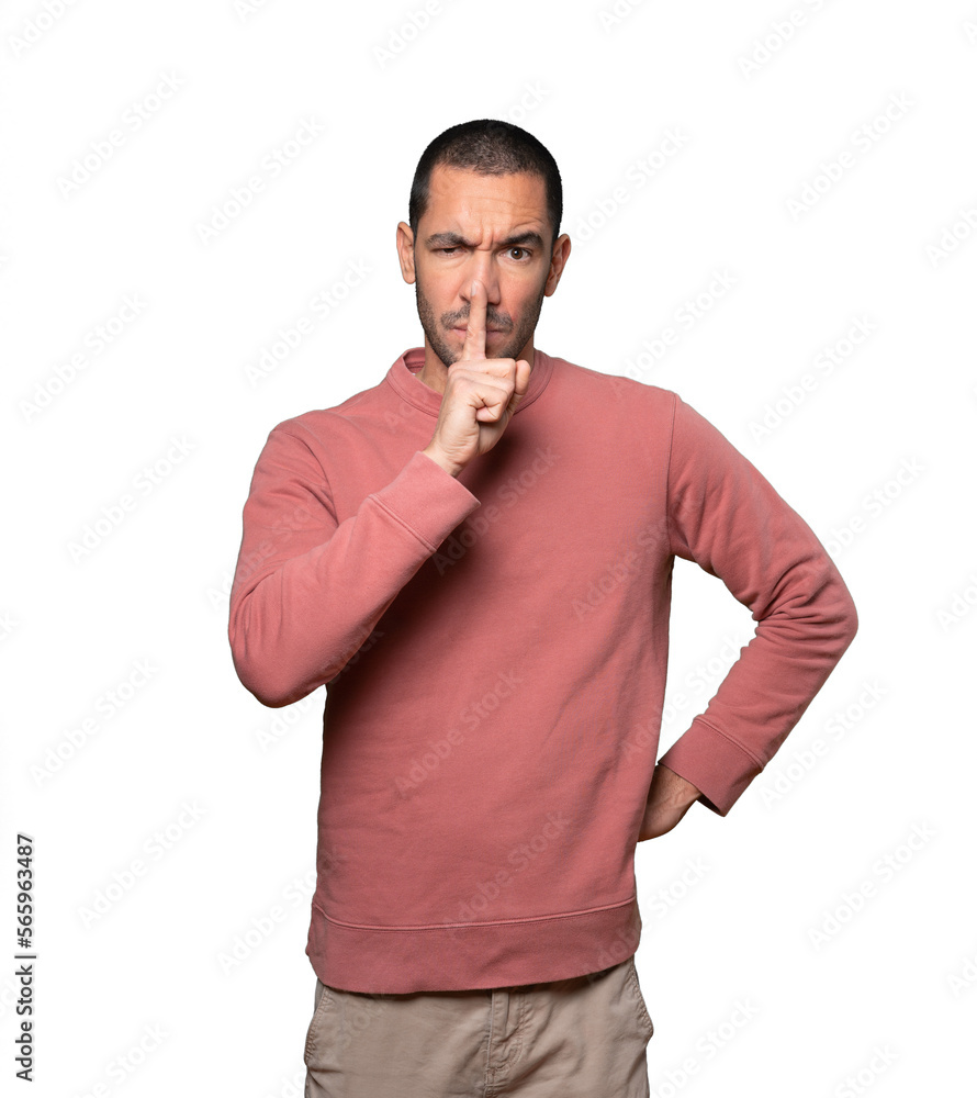 Serious young man asking for silence gesturing with his finger Serious young man asking for silence gesturing with his finger